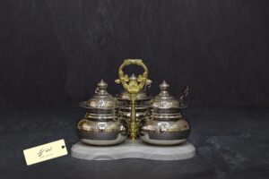 ست ادویه دو تایی کروم سویل شامل دو ظرف کروم با درپوش و قاشق، روی پایه چوبی با دسته طلایی تزئینی